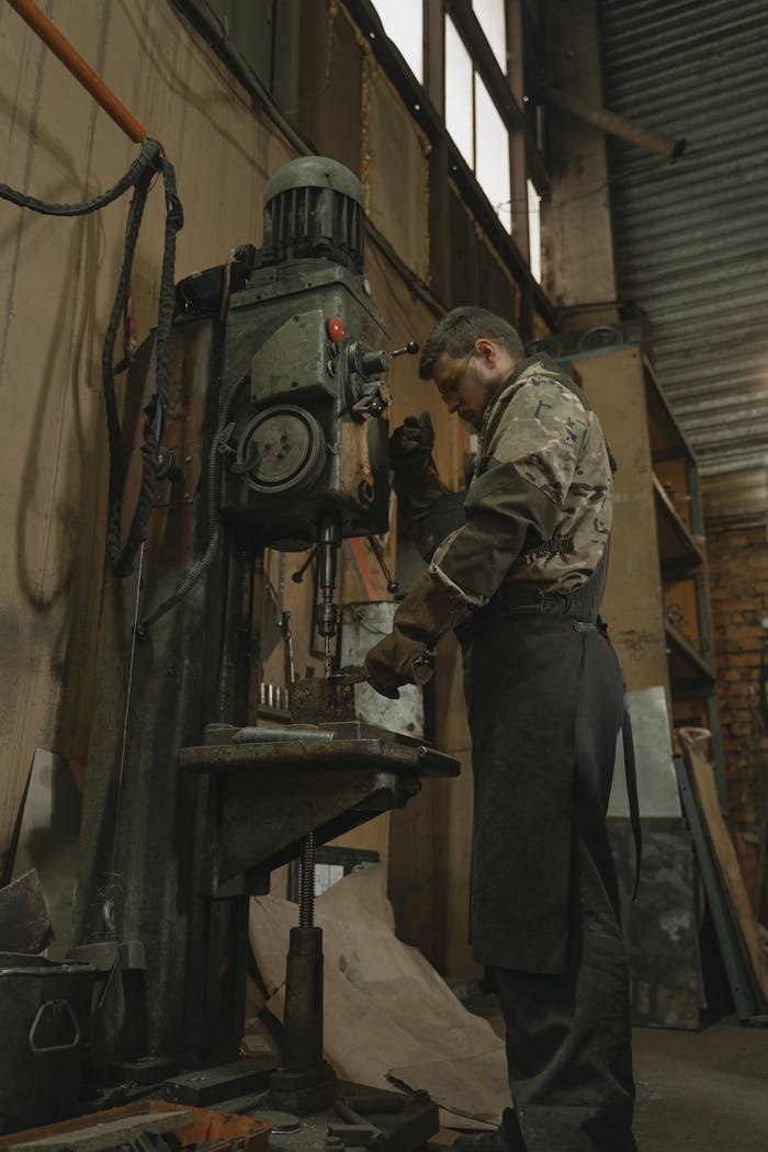 Skilled craftsman using a drilling machine in an industrial workshop setting.